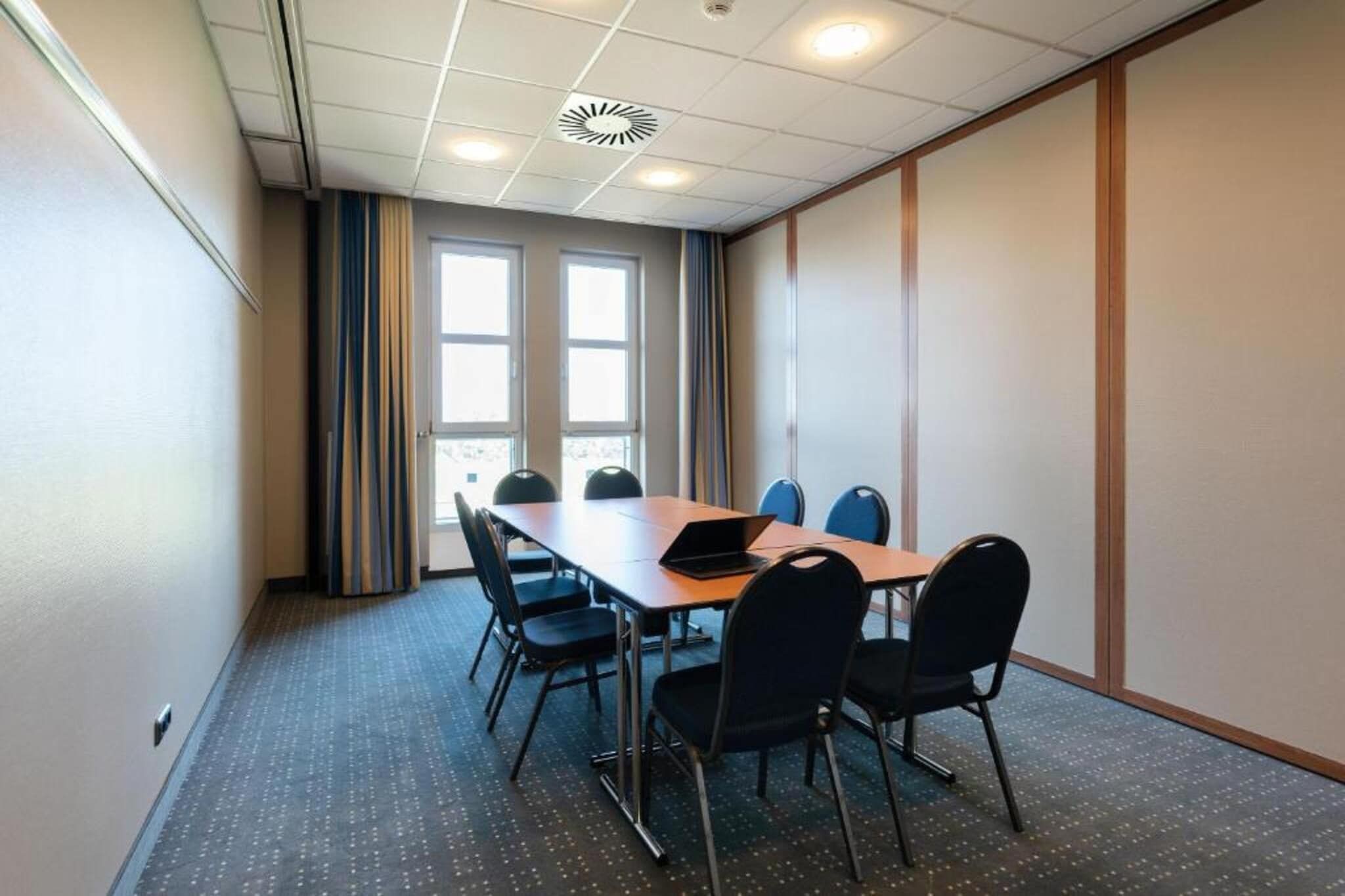 Ein Konferenzraum mit einem langen Tisch, sechs Stühlen und einem Laptop auf dem Tisch.