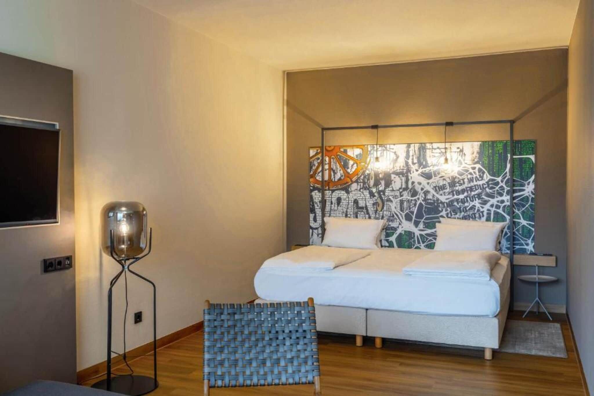 A modern bedroom with a bed, a floor lamp, a woven rug, and a wall with abstract art.