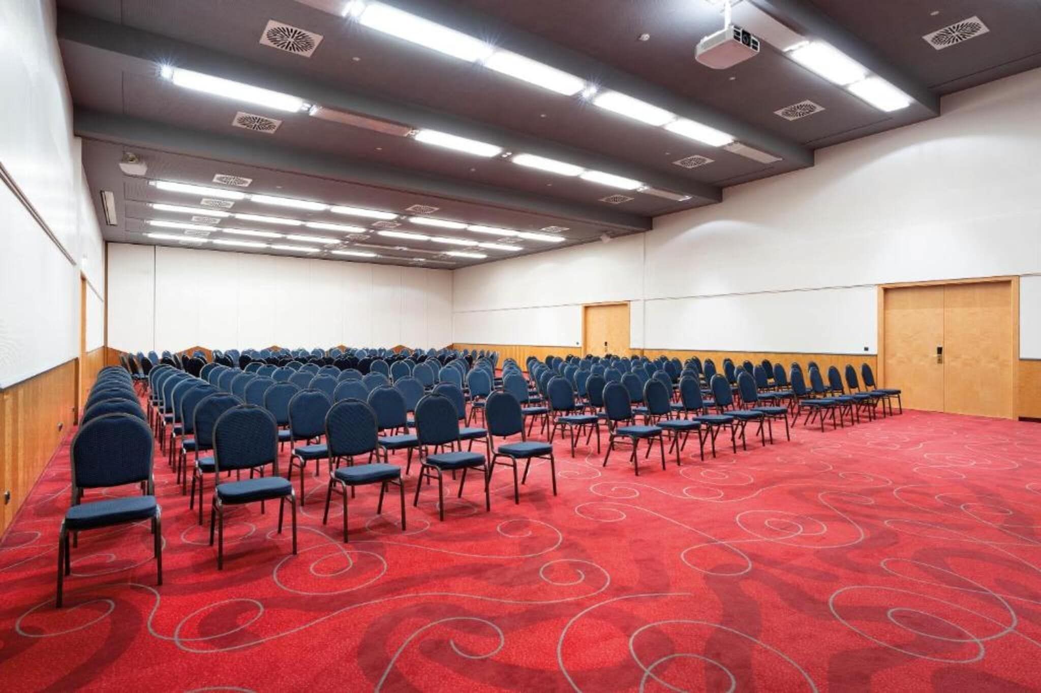 Un salón de conferencias con hileras de sillas, alfombra roja y una pizarra.