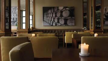Een restaurantinterieur met een rij barkrukken, een wijnvattenwand en een kaars op de tafel.