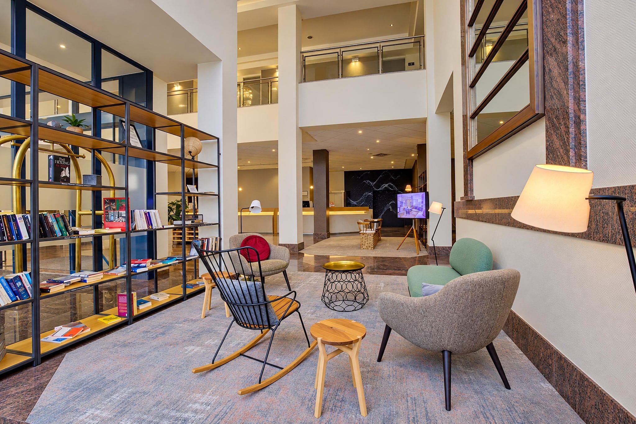 A spacious lobby with a modern design, featuring a seating area with chairs and a sofa, a bookshelf, and a television screen.