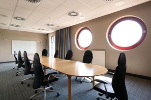 A conference room with a long table, multiple chairs, a whiteboard, and two large windows with circular frames. - Hotel Nürnberg- Suite (Nuremberg)