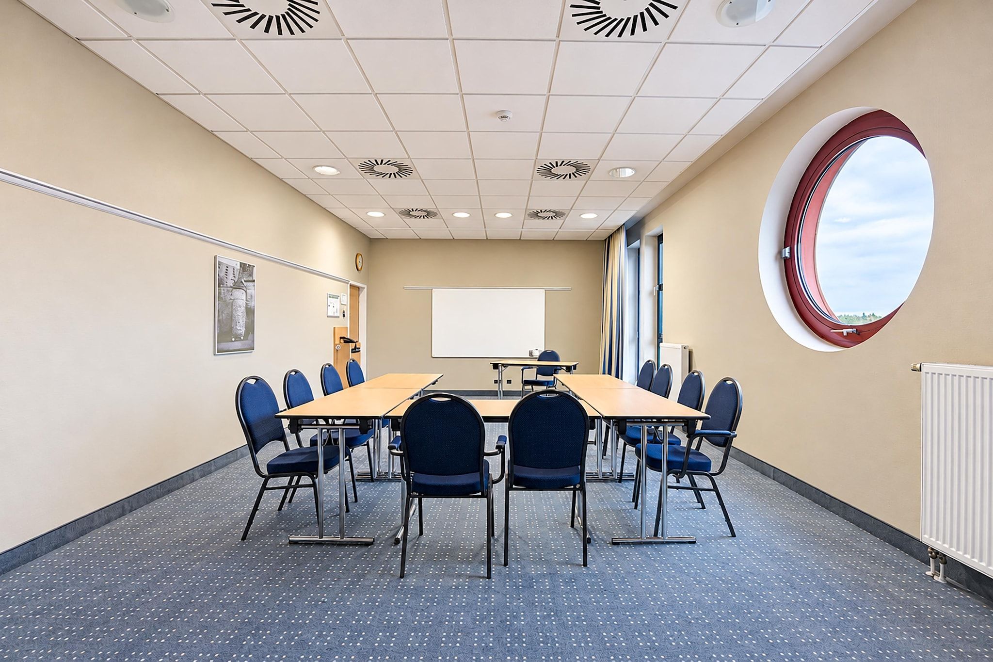 A conference room with a long table, chairs, a projector screen, and a large window.