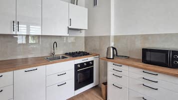 Une cuisine moderne avec des meubles blancs, un évier en acier inoxydable, une cuisinière à gaz, un four et un four à micro-ondes.