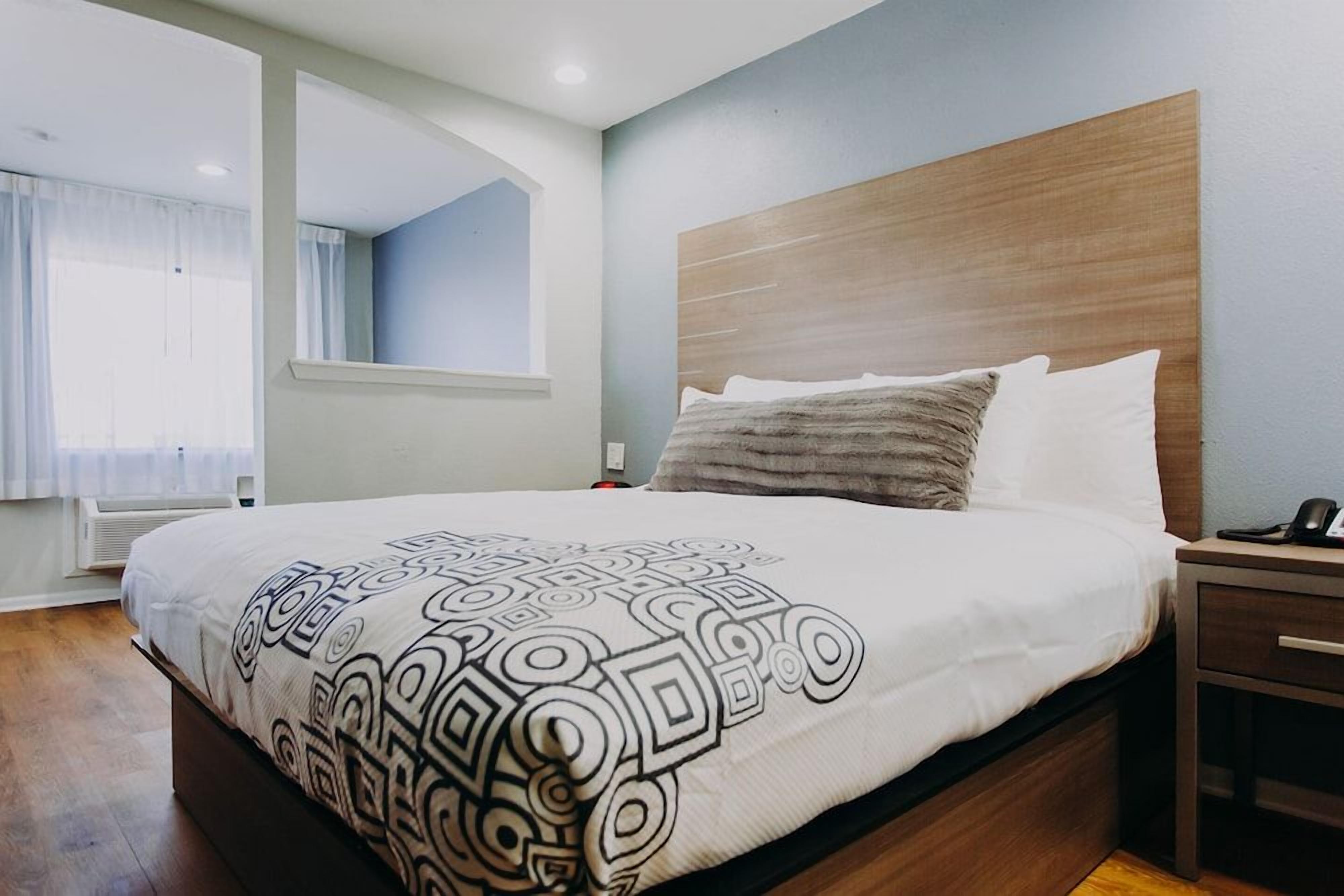 Una cama bien hecha con una manta estampada, un cabecero de madera y una mesita de noche con un teléfono.