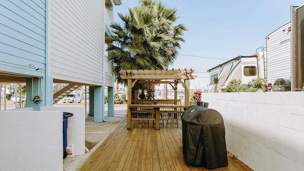 A wooden deck with a wooden pergola, a barbecue grill, and a white RV parked in the background. - Passport Inn (Kemah)