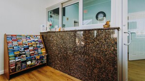 A reception desk with a display of magazines and a clock on the wall. - Passport Inn (Kemah)