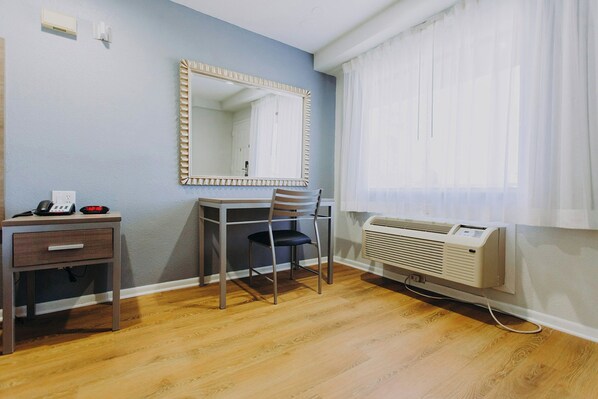 A room with a desk, chair, mirror, and a window with curtains. - Passport Inn (Kemah)