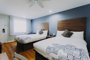 A hotel room with two beds, a ceiling fan, a wooden headboard, and a window with curtains. - Passport Inn (Kemah)