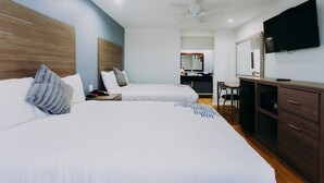 A hotel room with two beds, a desk, a chair, a television, and a ceiling fan. - Passport Inn (Kemah)