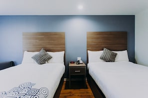 A hotel room with two beds, a nightstand with a phone and a clock, and a wooden headboard.