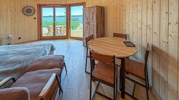 Une pièce comprenant un lit, une table ronde en bois avec des chaises, une armoire et une vue sur une étendue d’eau, visible à travers des portes vitrées.