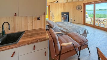 Interior em madeira com cozinha, uma cama e vista para um lago através de grandes janelas.