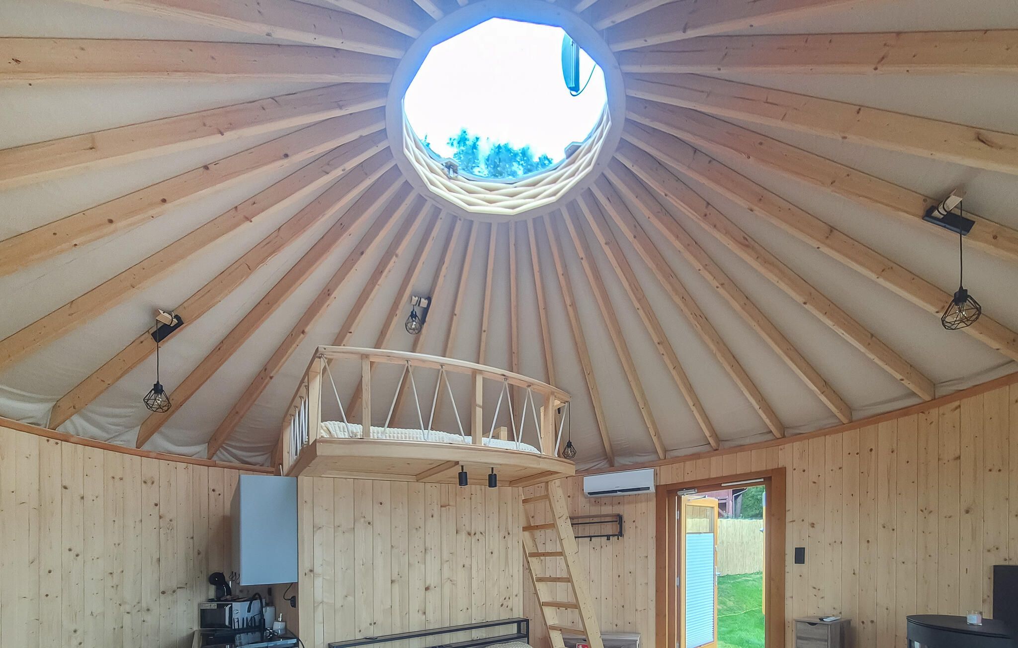 Un intérieur en bois avec une lucarne centrale, un lit en mezzanine et une échelle menant à celle-ci.