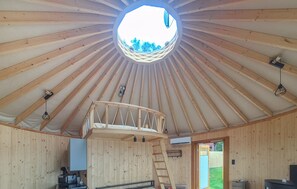 Un intérieur en bois avec une lucarne centrale, un lit en mezzanine et une échelle menant à celle-ci.