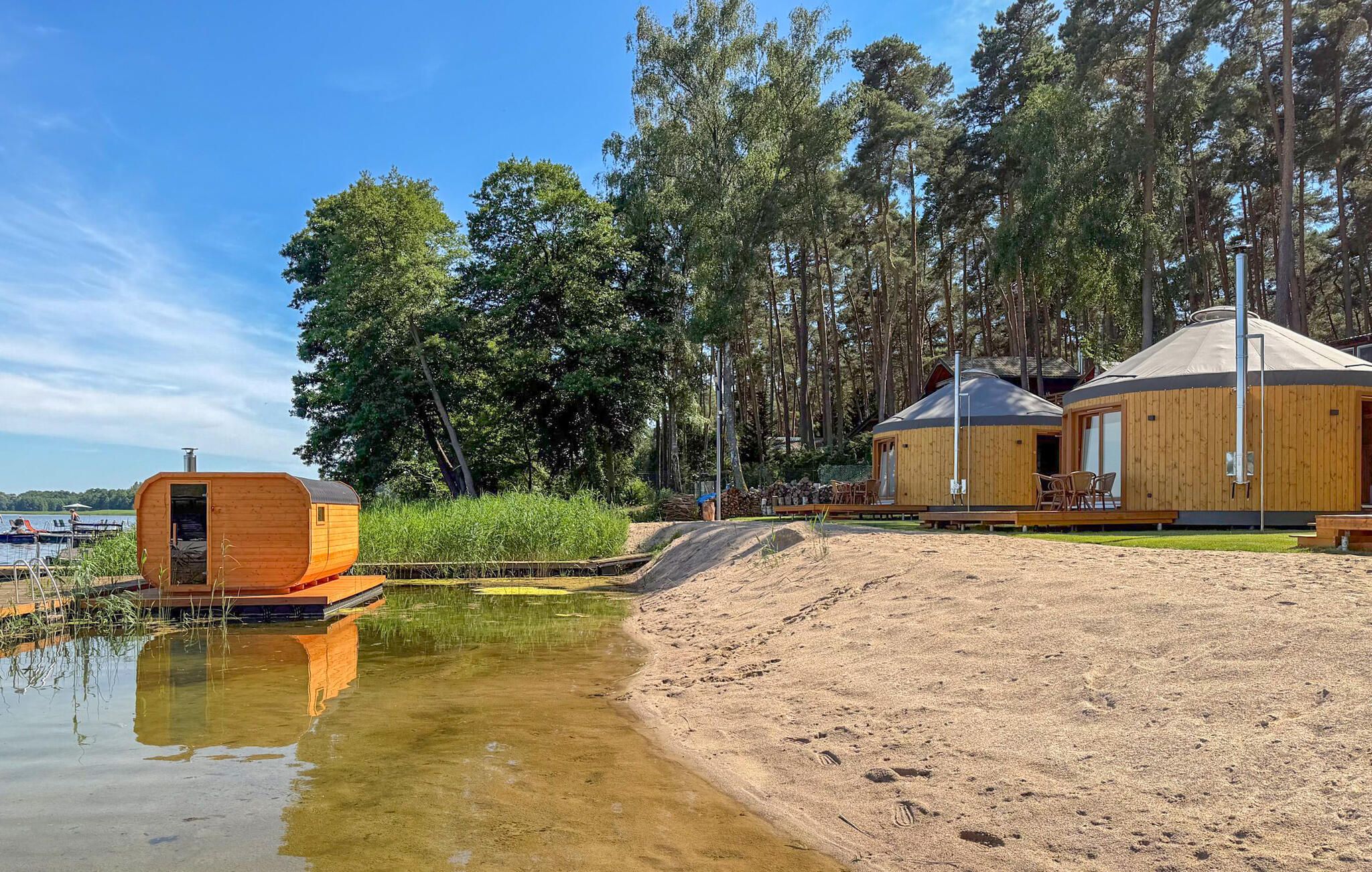 Une yourte dotée d’un porche couvert et d’une petite construction en bois située près d’un plan d’eau.