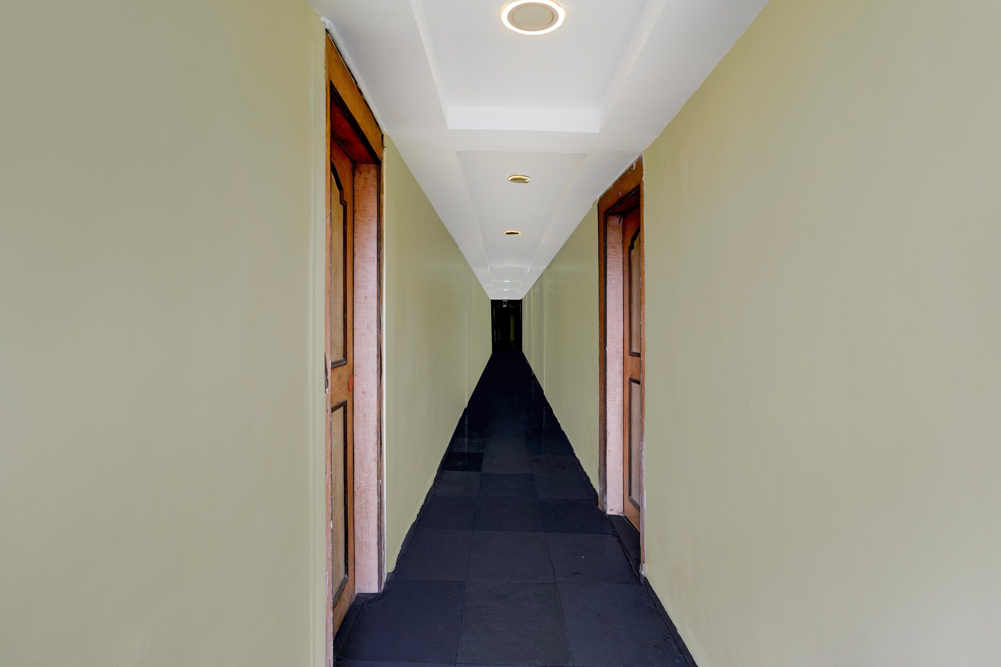 A corridor with a dark floor, light walls, and wooden doors on either side.
