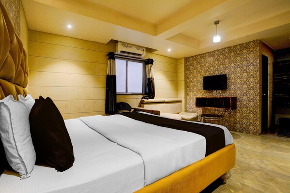 A hotel room with a bed, a television, a window with curtains, and a patterned wall.
