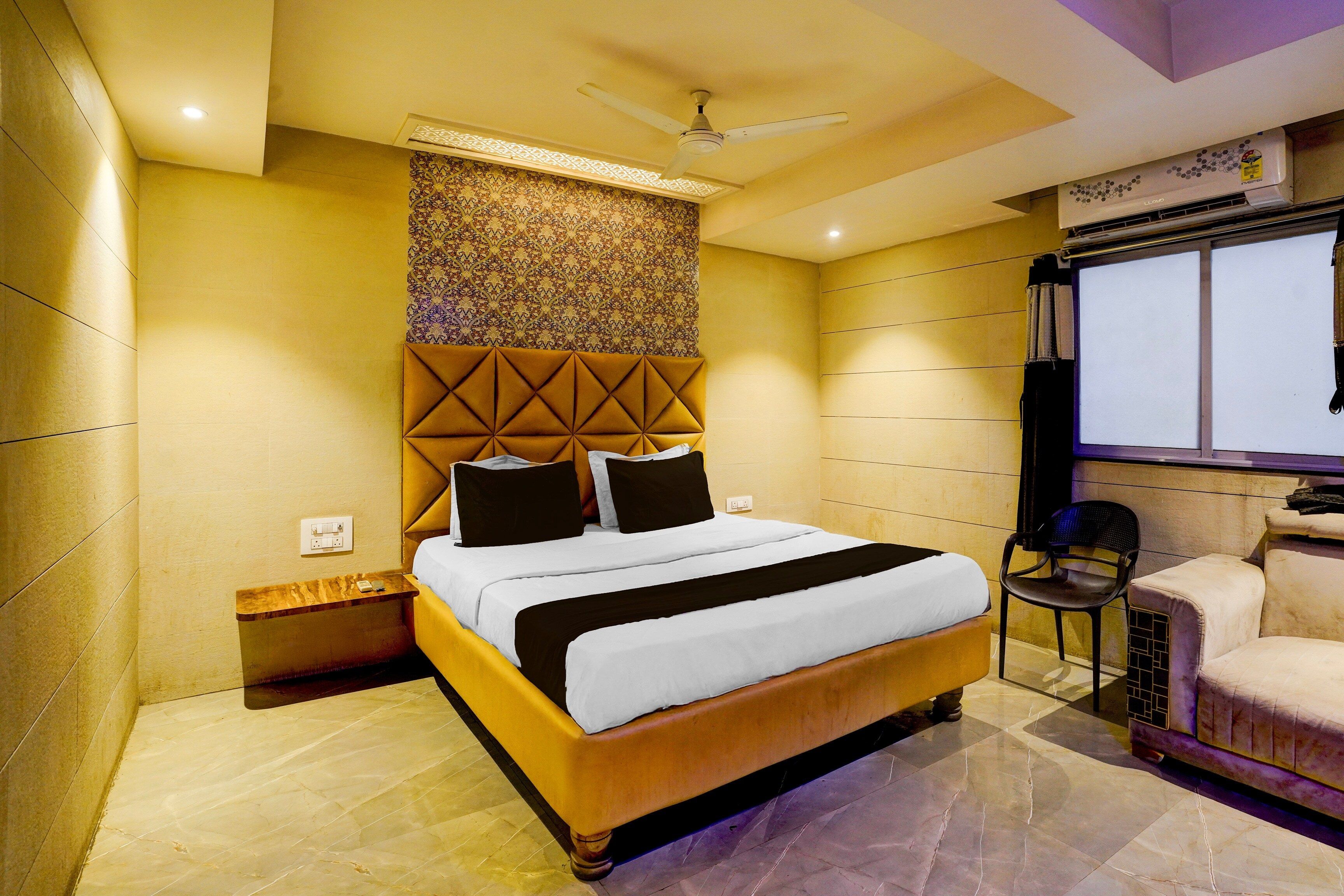A hotel room with a bed, a ceiling fan, a window, and a seating area with a chair.