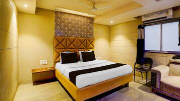 A hotel room with a bed, a ceiling fan, a window, and a seating area with a chair.