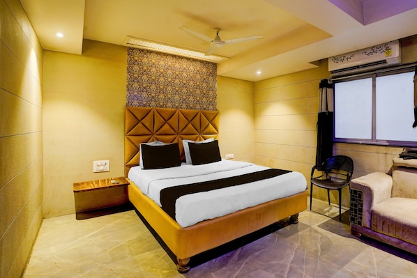 Habitación de hotel con cama, ventilador de techo, ventana y zona de estar con una silla.