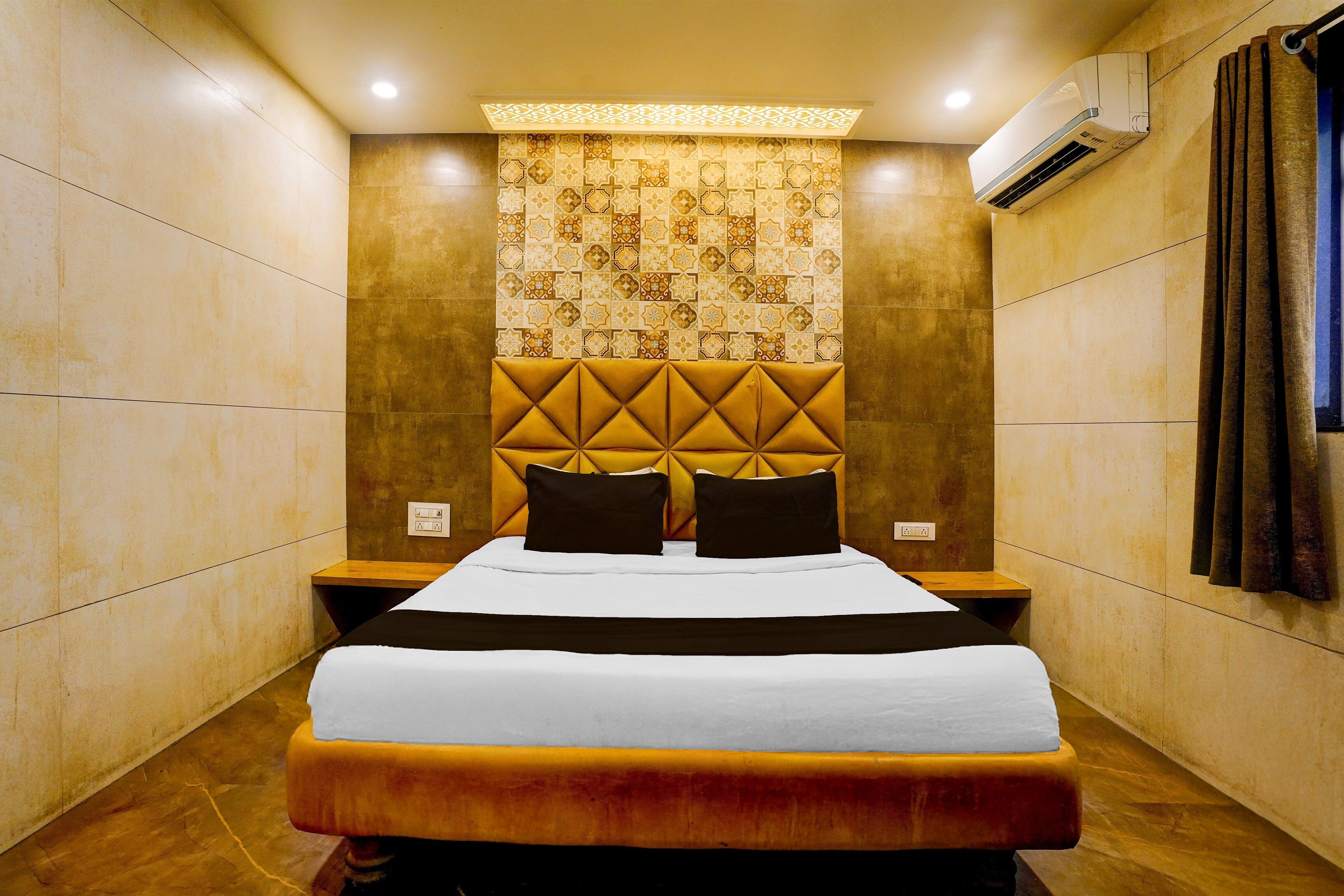 Habitación de hotel con una cama grande, cabecera con diseño geométrico, aire acondicionado de pared y un tapiz decorativo sobre la cama.