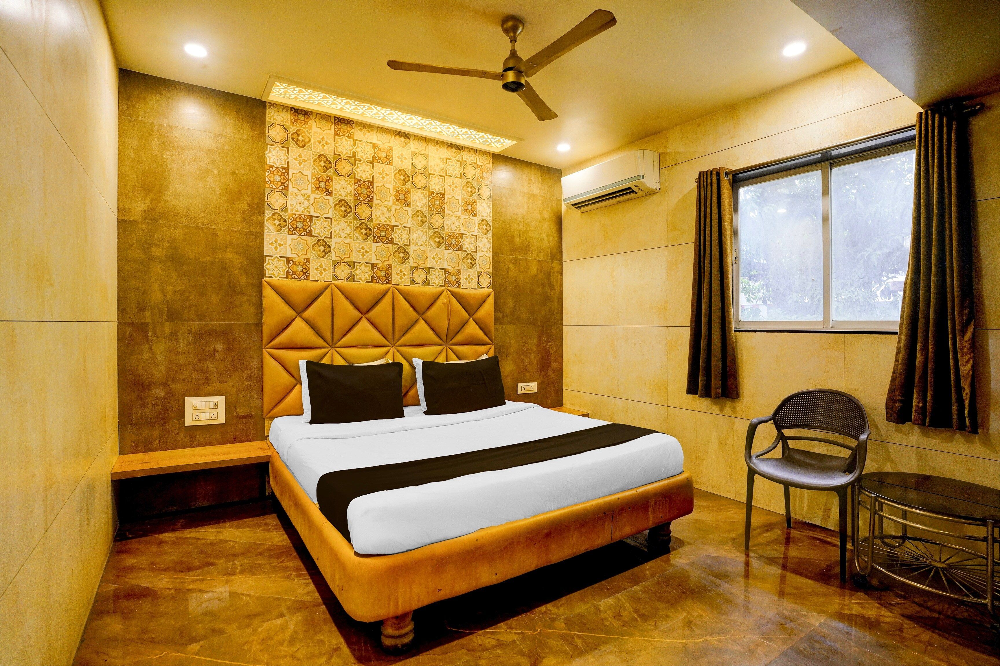 A hotel room with a bed, a chair, a ceiling fan, an air conditioning unit, and a window with curtains.