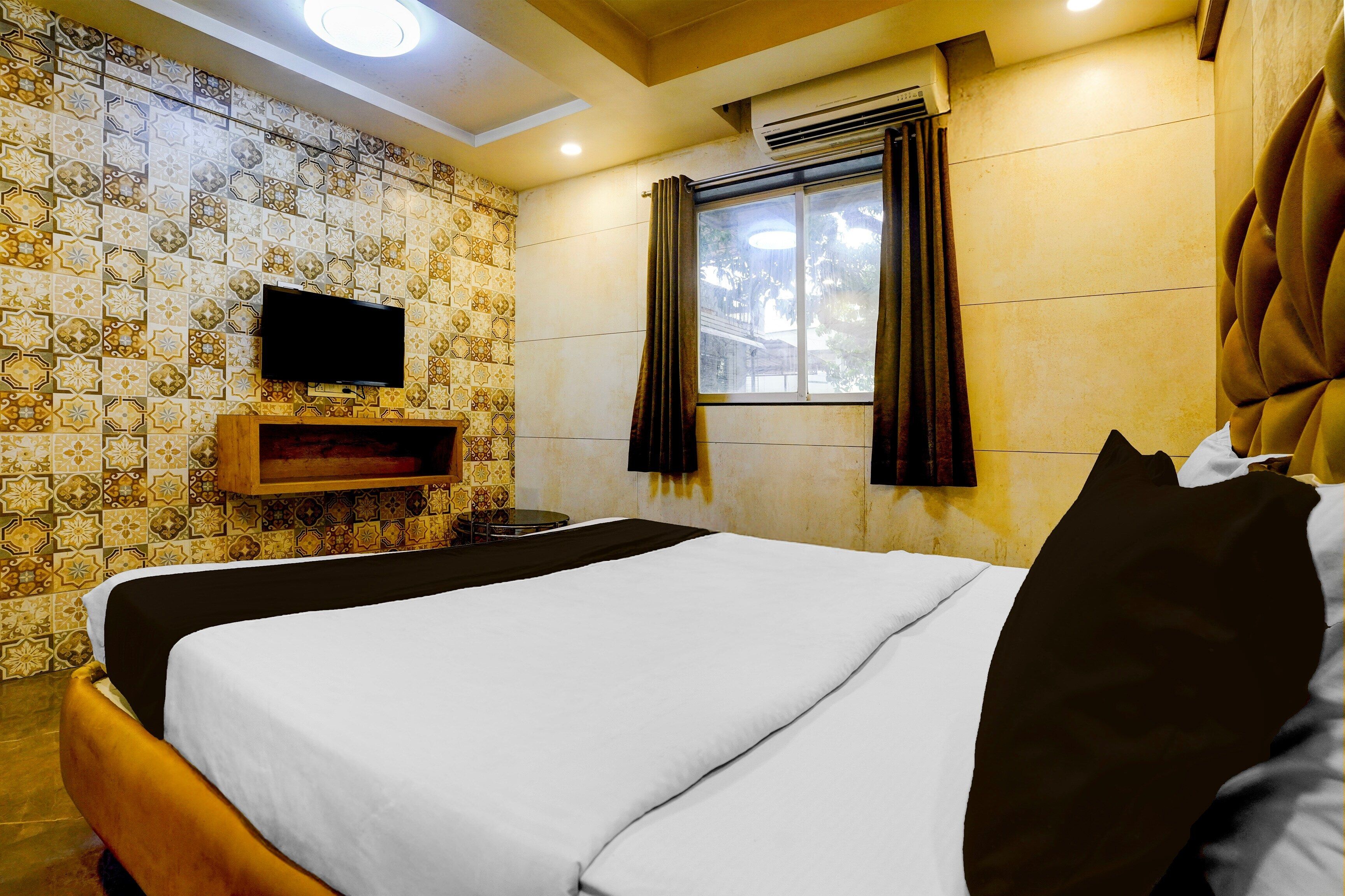 Une chambre d’hôtel avec un lit, un téléviseur à écran plat fixé au mur, une fenêtre avec des rideaux et un papier peint à motifs.
