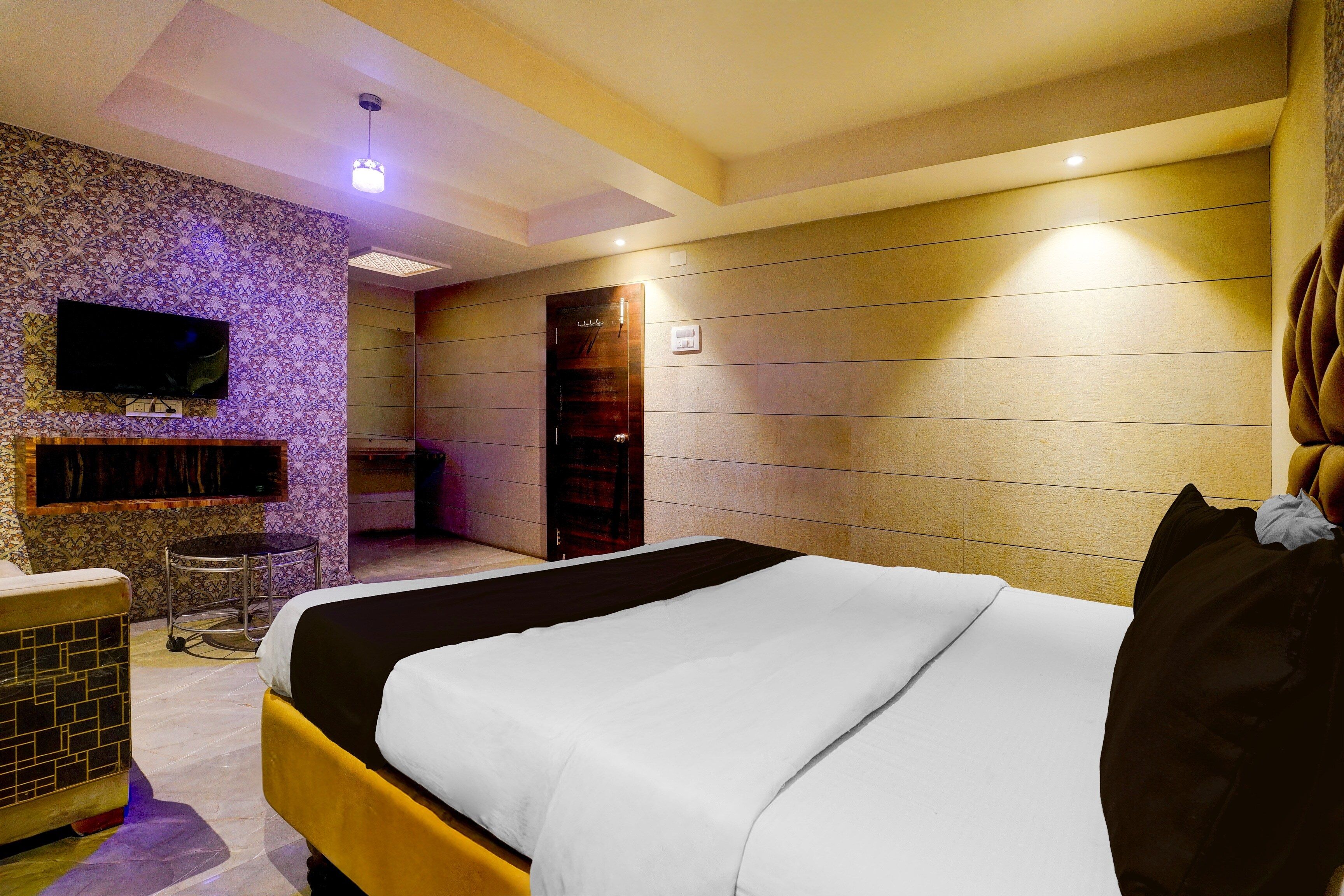 A hotel room with a bed, a television, a small bar area, and a bathroom.