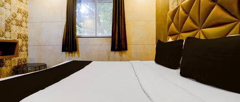 A hotel room with a large bed, a window with curtains, a wall air conditioner, and a patterned wall.