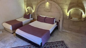 A room with two beds, each with a headboard and pillows, and a decorative wall with a circular emblem. - Dede Hostel Pansiyon (Ürgüp)