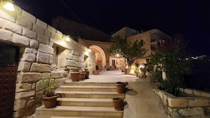 A stone building with a staircase leading to a door, surrounded by potted plants. - Dede Hostel Pansiyon (Ürgüp)