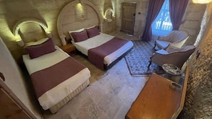 A room with two beds, a wooden nightstand, a chair, and a stone wall. - Dede Hostel Pansiyon (Ürgüp)