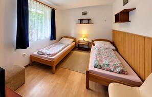 A bedroom with two wooden beds, a bedside table with a lamp, a small shelf, and a window with curtains. - 2 bedroom beautiful home in Przewloka (Przewloka)