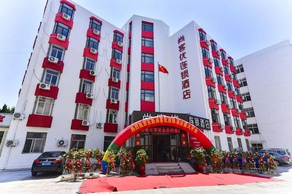 Un edificio de hotel de varios pisos con fachada roja y blanca, unidades de aire acondicionado y un toldo rojo con adornos florales.