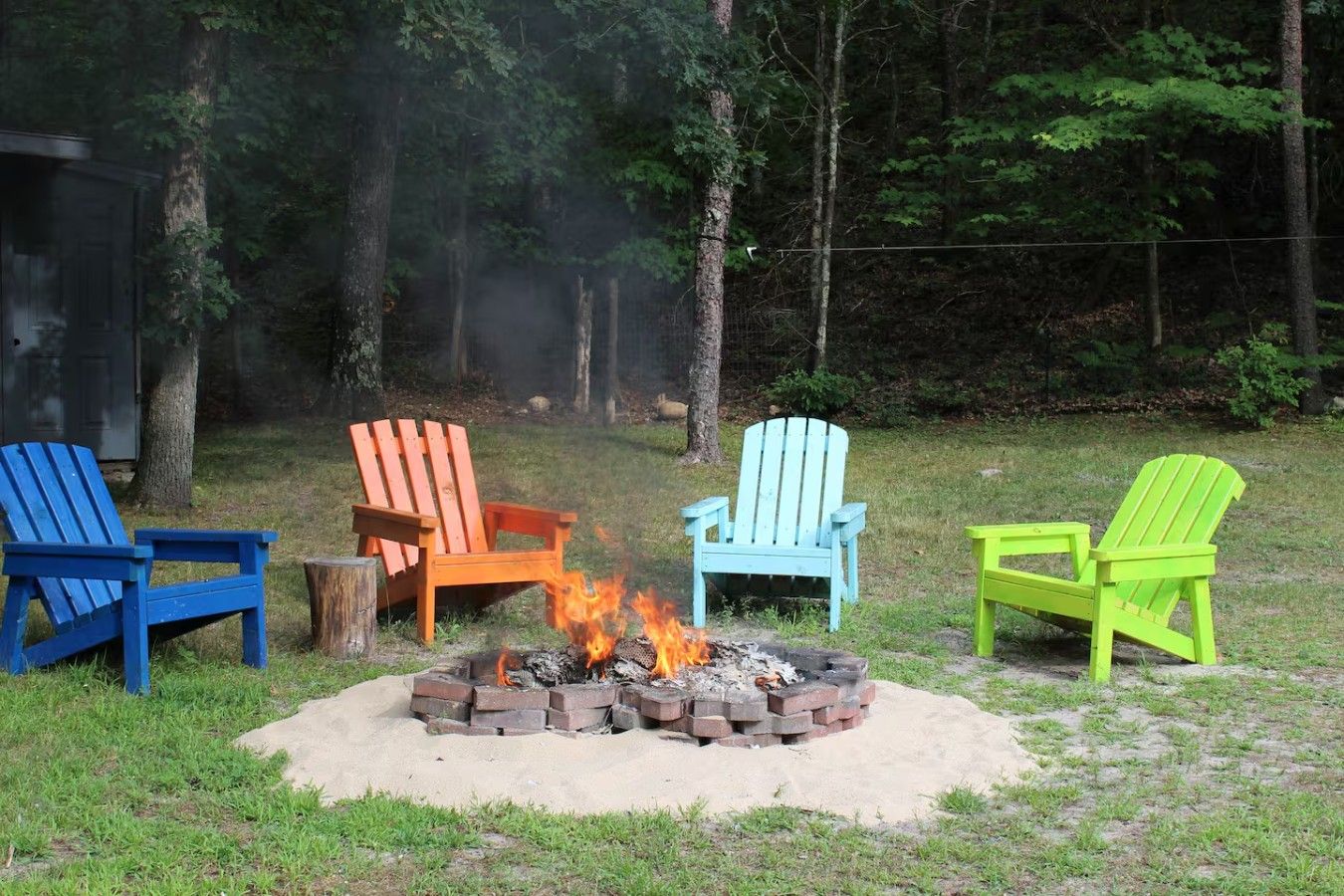 Een vuurkorf met vier Adirondack stoelen in verschillende kleuren.