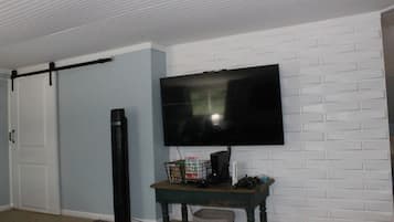 A room with a flat-screen TV mounted on a brick-patterned wall, a sliding door, a tall black speaker, and a small table with a basket.