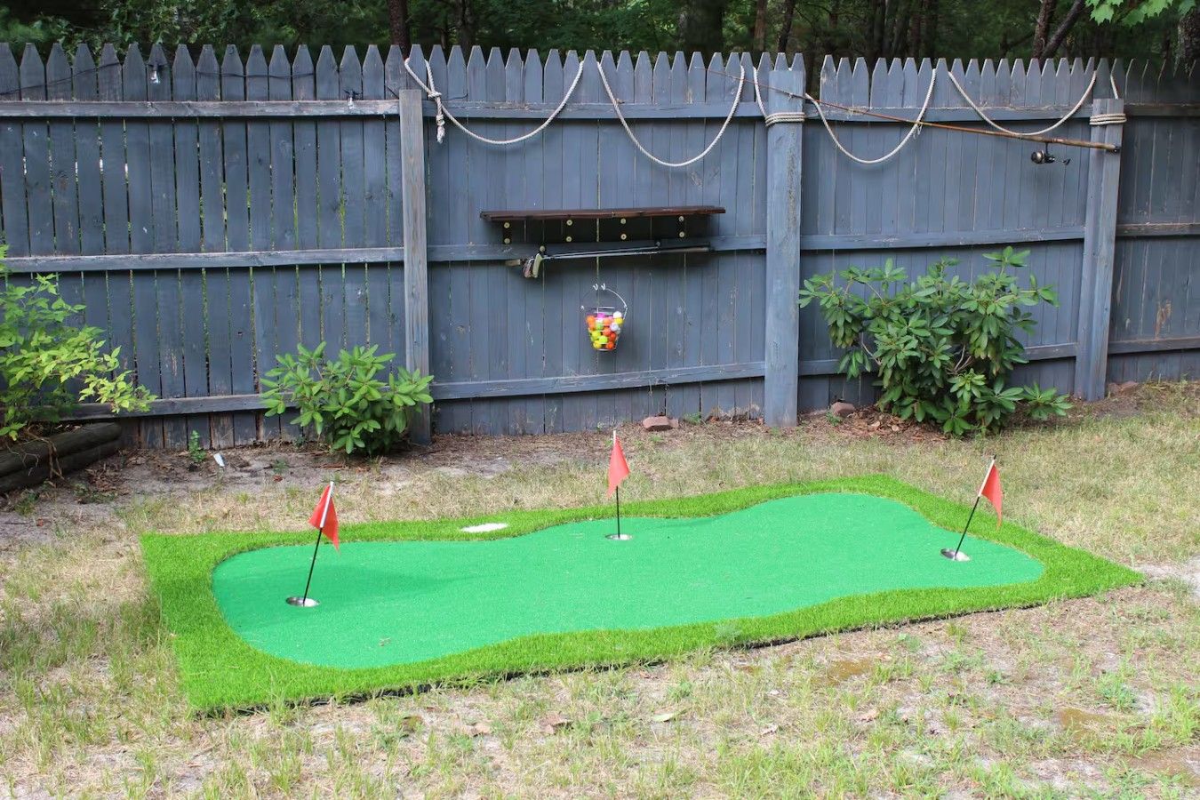 Um campo de mini golfe com três buracos, cerca de madeira e um comedouro para pássaros.