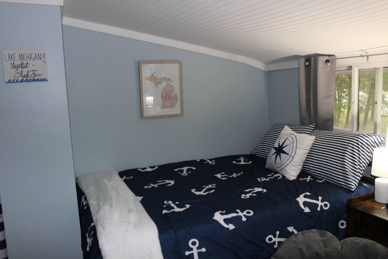 Une chambre à coucher avec un lit agrémenté de linge de lit sur le thème de la marine, une carte encadrée au mur et une fenêtre avec des rideaux.