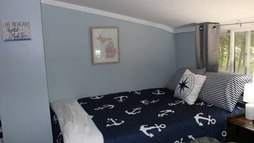 Une chambre à coucher avec un lit agrémenté de linge de lit sur le thème de la marine, une carte encadrée au mur et une fenêtre avec des rideaux.