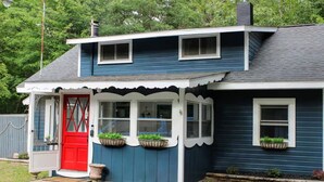Una casa de dos pisos con puerta roja, detalles blancos y varias ventanas.