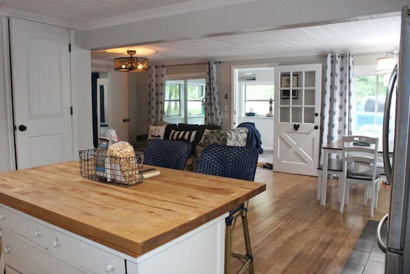A kitchen with a wooden countertop, a basket of snacks, and a dining area with a table and chairs.