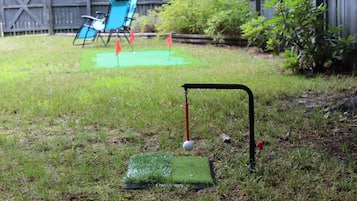 Een achtertuin met een putting green, een golfbal en een vlaggenstok.