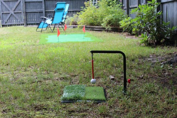A backyard with a putting green, a golf ball, and a flagstick.