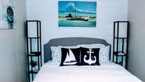 Una cama con una colcha blanca y dos almohadas, una con un diseño de velero y la otra con un ancla.