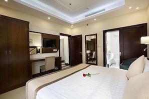 A hotel room with a large bed, a desk, a chair, a TV, and a bathroom visible through an open door. - Sun Park Hotel Apartments (Jeddah)