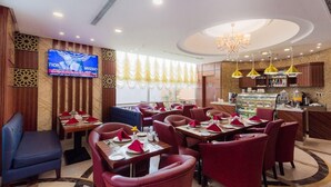 En restaurang med röda stoppade stolar, en bardisk och en tv-skärm som visar en sportevenemang.