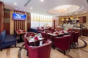 A restaurant with red upholstered chairs, a bar area, and a television screen displaying a sports event. - Sun Park Hotel Apartments (Jeddah)