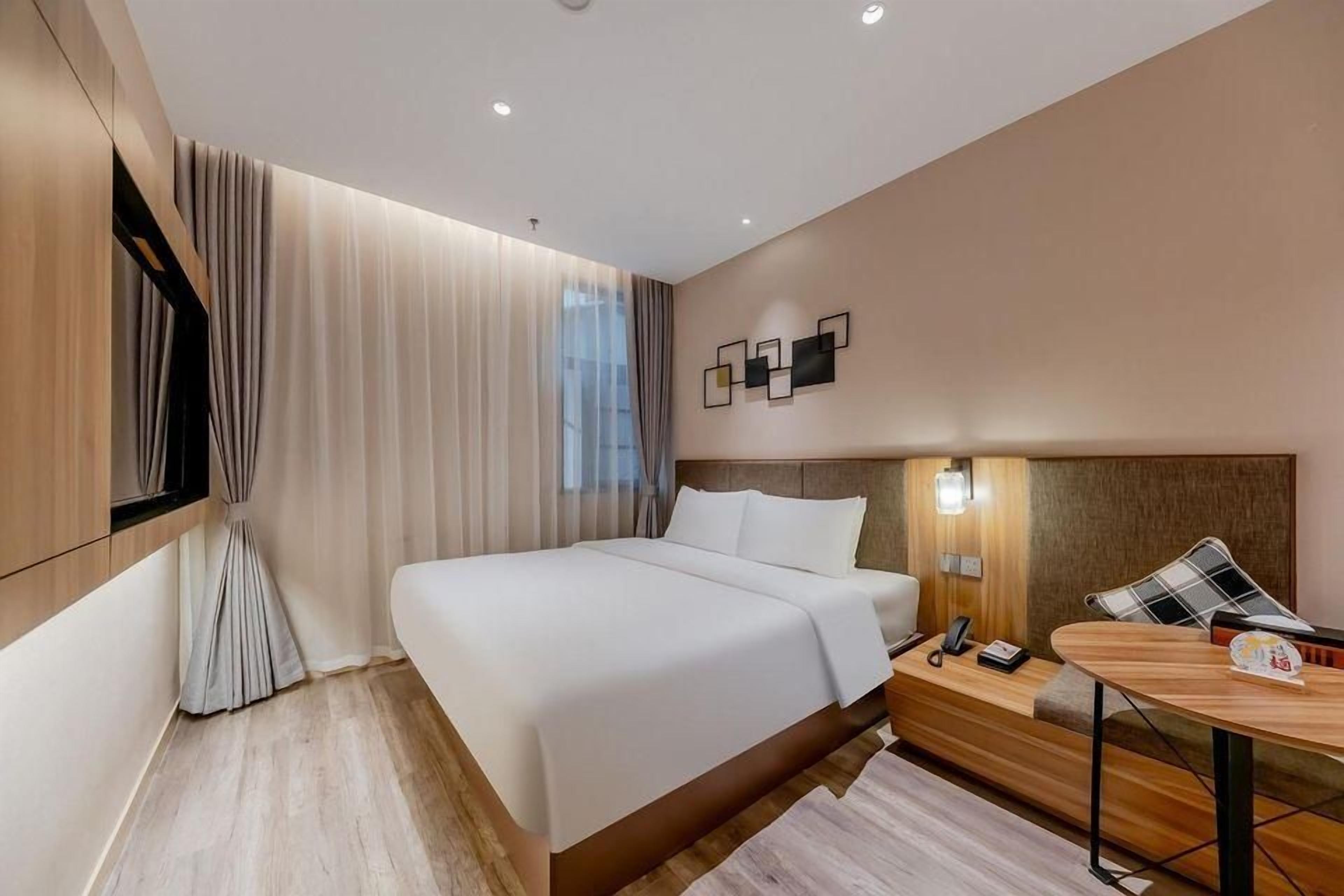 Una habitación de hotel moderna con una cama grande, una mesita de noche con lámpara y vistas a la ciudad.