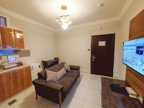 A living room with a sofa, a television, a wooden cabinet, and a ceiling light fixture. - Iwan Alandalusia Hotel Suites Alrehab (Jeddah)